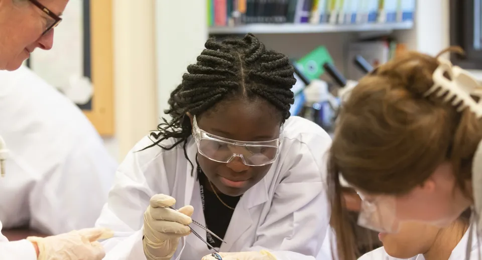 Una studentessa in camice bianco esamina un'altra studentessa con le trecce in un laboratorio della Rye St. Antony School.