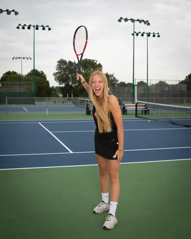 Studentessa in divisa sportiva esulta con la racchetta alzata su un campo da tennis scolastico negli USA