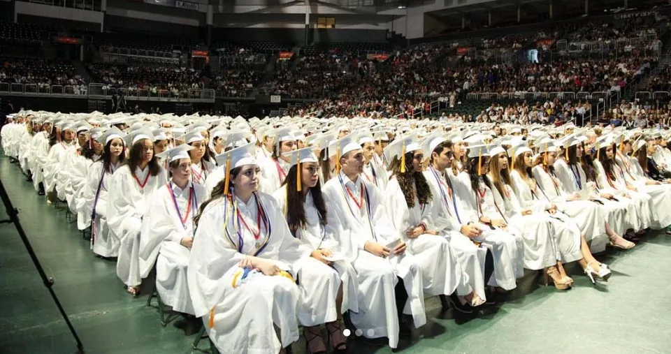 Studenti della Miami Beach Senior High School indossano toghe bianche durante una cerimonia di diploma in una sala.