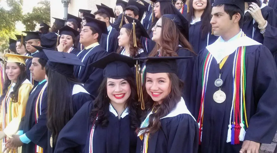 Un gruppo di diplomati della St. John Paul II High School sta all'aperto in abito accademico e sorride alla telecamera.