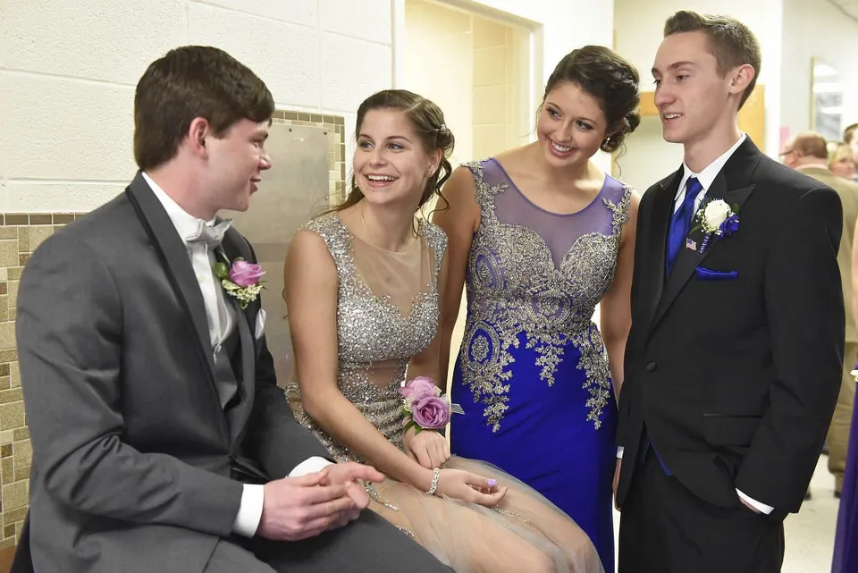 Quattro studenti della Queensbury High School sono in piedi nel corridoio con abiti eleganti durante un ballo scolastico.