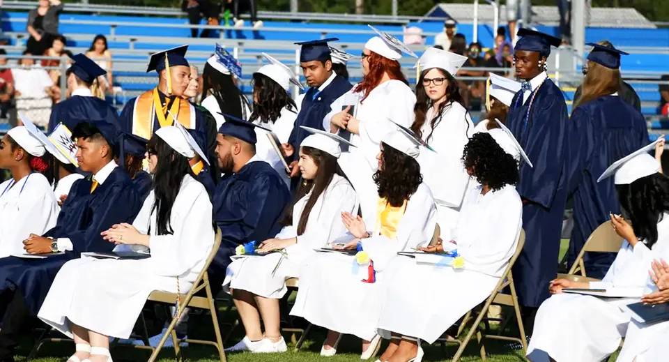 Un gruppo di diplomati e diplomate della Seaford Head School si trova all'aperto in abito accademico con tocco in una giornata soleggiata.