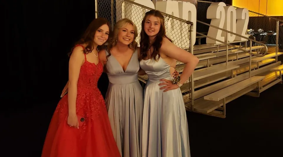 Tre studentesse della All Saints High School Calgary posano insieme su una tribuna all'aperto.