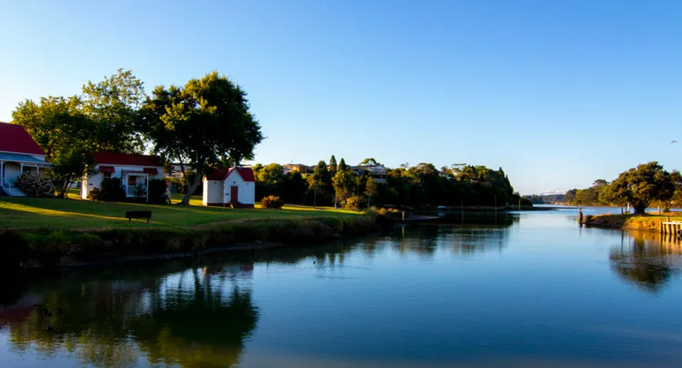 Un tranquillo corso d'acqua con edifici colorati e alberi si riflette nell'acqua nella tenuta del Waiuku College.