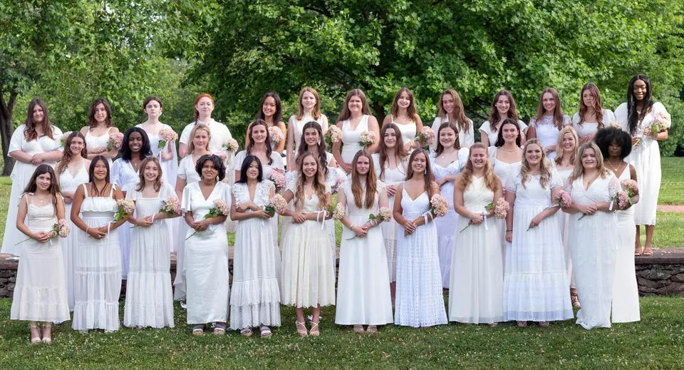 Un gruppo di studentesse della Foxcroft School indossa tuniche romane bianche e sta insieme nell'area verde esterna.
