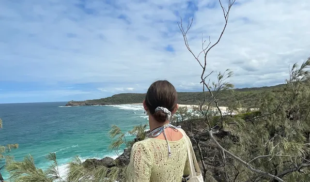 Chica de espaldas contemplando una bahía de aguas turquesas desde un mirador entre la vegetación
