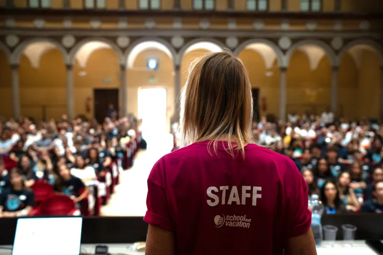 Membro dello staff in maglietta rossa con scritta «staff» rivolto verso il pubblico in sala