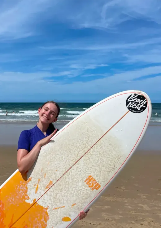 Antonia lächelt mit einem Surfbrett am Strand in Australien