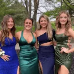 Cuatro jóvenes sonrientes posan al aire libre vestidas con elegantes vestidos de gala