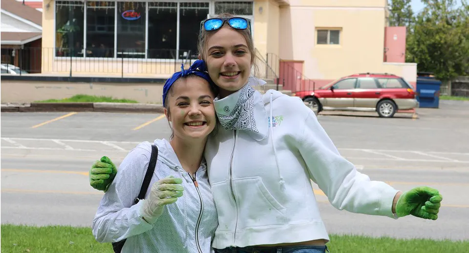 Due studentesse della Banting Memorial High School sono in piedi davanti a un edificio con auto parcheggiate sullo sfondo.