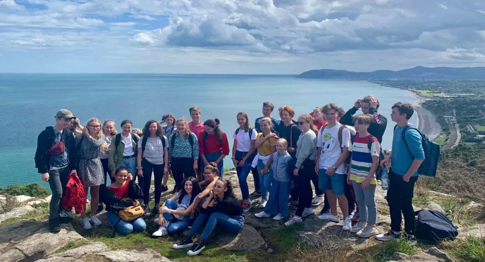 Studenti della Mercy Secondary School si trovano su una roccia e osservano il paesaggio costiero con acqua e montagne.