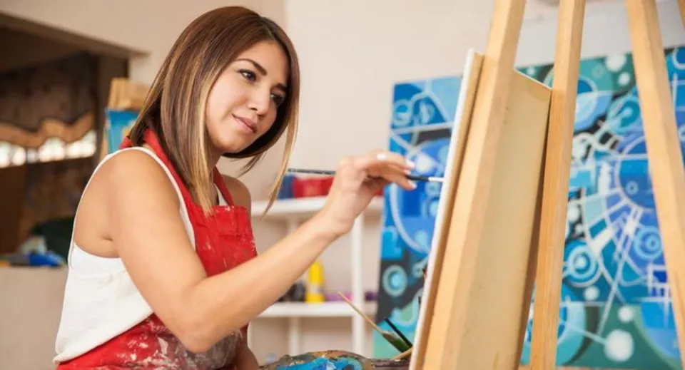 Una studentessa della Ribet Academy dipinge su una tela in un atelier con vivaci quadri astratti alle pareti.
