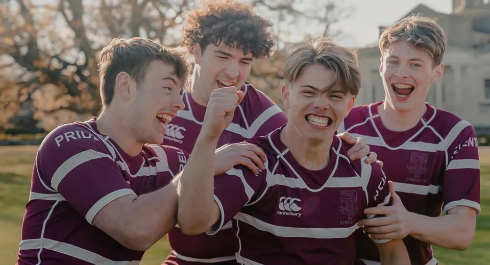 Un gruppo di quattro studenti della Haileybury School in divisa da rugby posa in un'area esterna alberata.