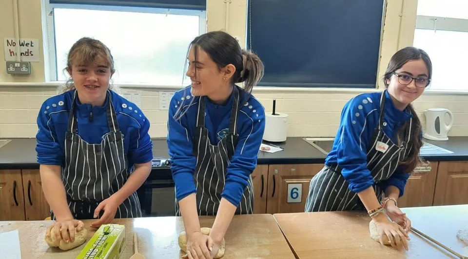 Tre studenti dell'Iascaigh College in divisa blu sono in piedi vicino a un tavolo in una classe con una lavagna sullo sfondo.