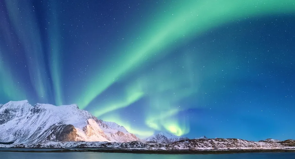 Montagne innevate con l'aurora boreale verde e blu nel cielo notturno vicino alla Tecumseh Vista Academy.