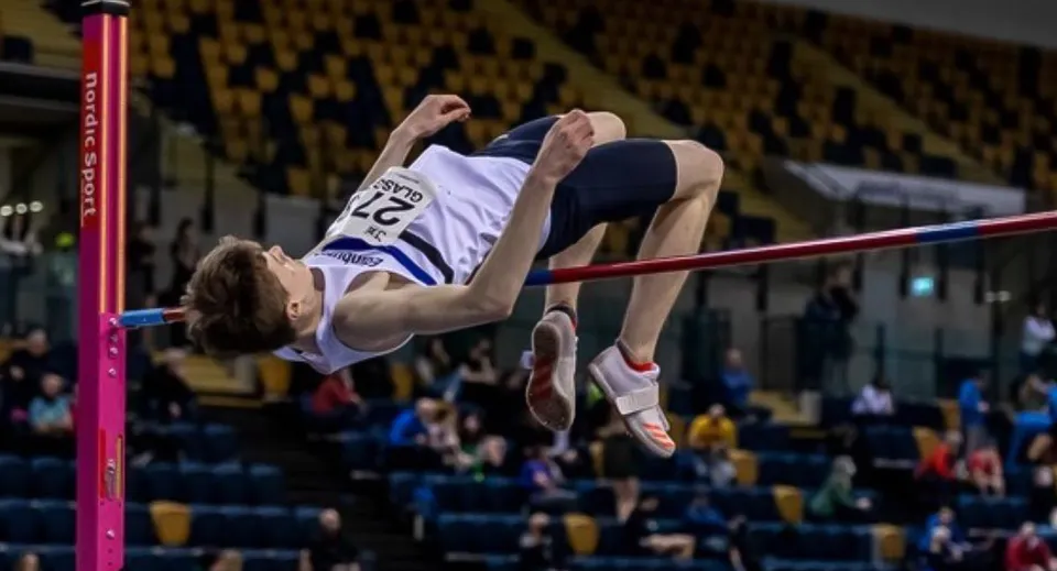 Un atleta della Firrhill High School esegue un salto in alto oltre l'asticella in una palestra con del pubblico.
