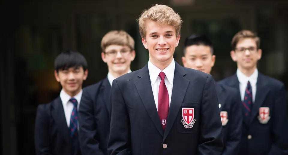 Un gruppo di studenti in divisa scolastica si trova insieme in una stanza formale nel campus della St. George’s School.