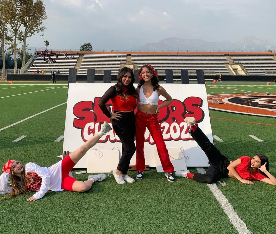 Due studentesse della Chaffey High School in posa davanti a un cartello del Sports Club 2022 sul campo sportivo con lo stadio sullo sfondo.