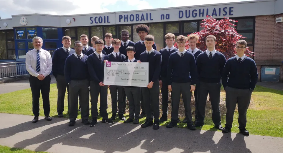 Studenti della Douglas Community School in divisa scolastica sono davanti all'edificio della scuola con in mano un grande assegno.