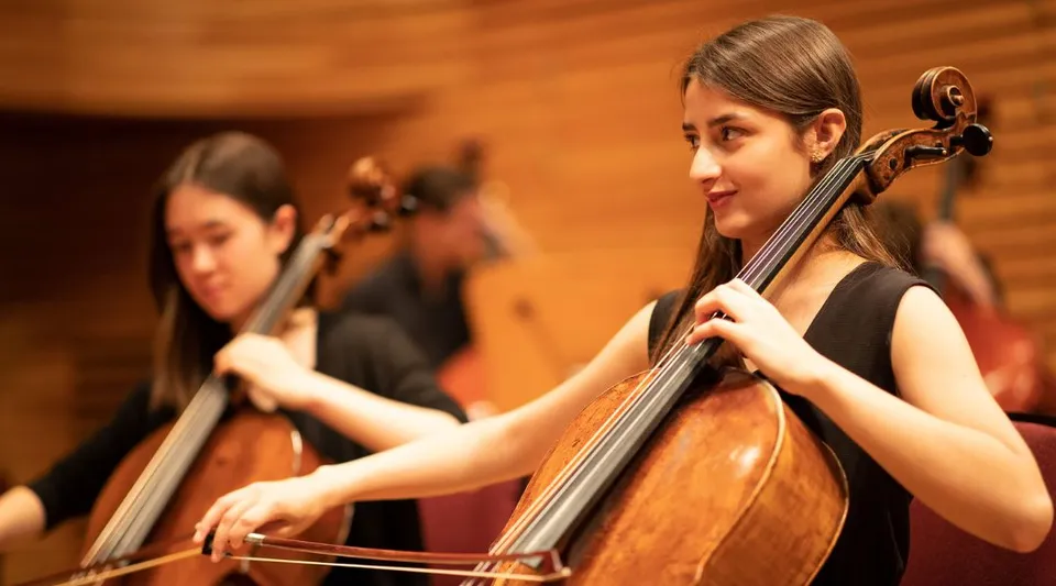 Una studentessa della Yehudi Menuhin School suona il violoncello sul palco con un altro musicista sullo sfondo.