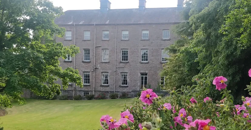 L'edificio in pietra della Royal School Armagh dietro un prato, circondato da alberi e fiori rosa.