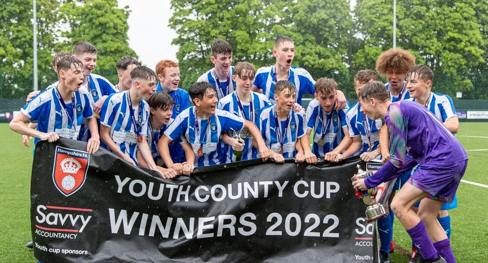 Un gruppo di studenti della Corfe Hills School è in piedi su un campo d'erba attorno a uno striscione per la vittoria della Youth County Cup 2022.