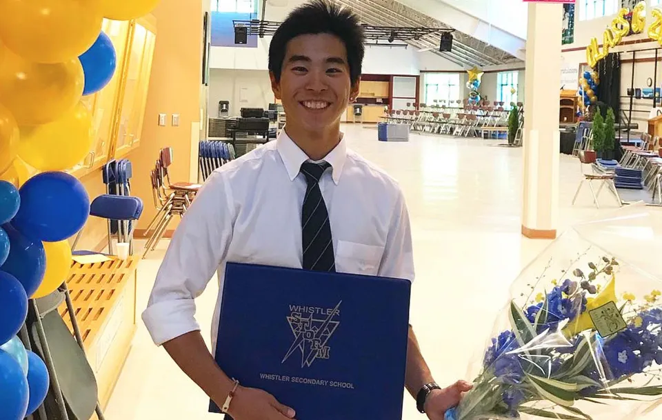 Uno studente sorridente della Whistler Secondary School si trova nel corridoio colorato con palloncini e tiene una cartella blu.