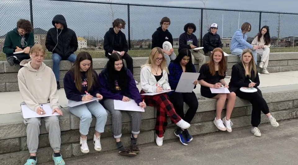 Un gruppo di studenti e studentesse siede su un muretto di cemento nell'area esterna della Maple Ridge Secondary School in Ontario.