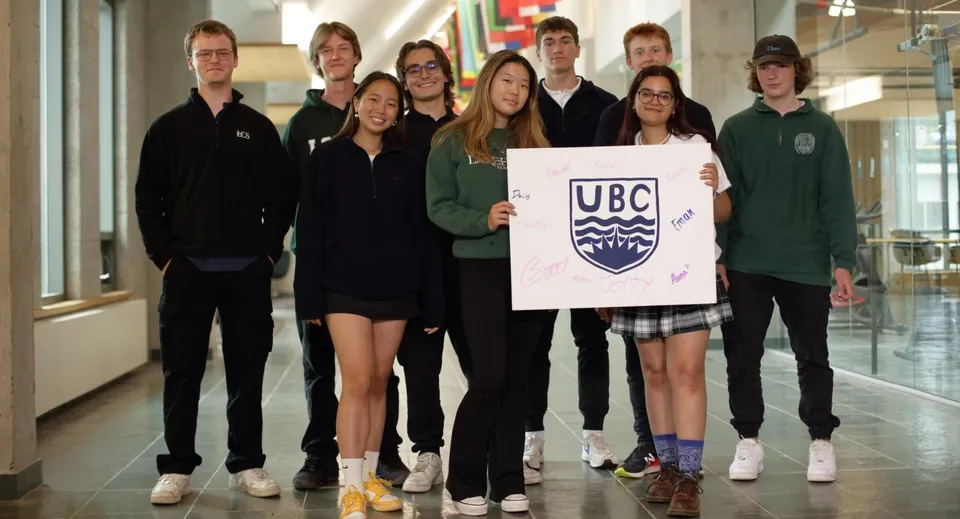 Un gruppo di studenti della Lakefield College School sta insieme in un edificio scolastico tenendo un cartello con il logo UBC.