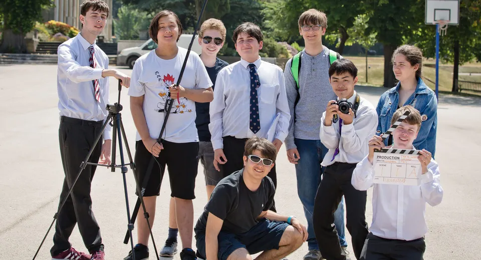 Un gruppo di studenti della Mill Hill School si trova insieme all'aperto vicino a un canestro da basket.