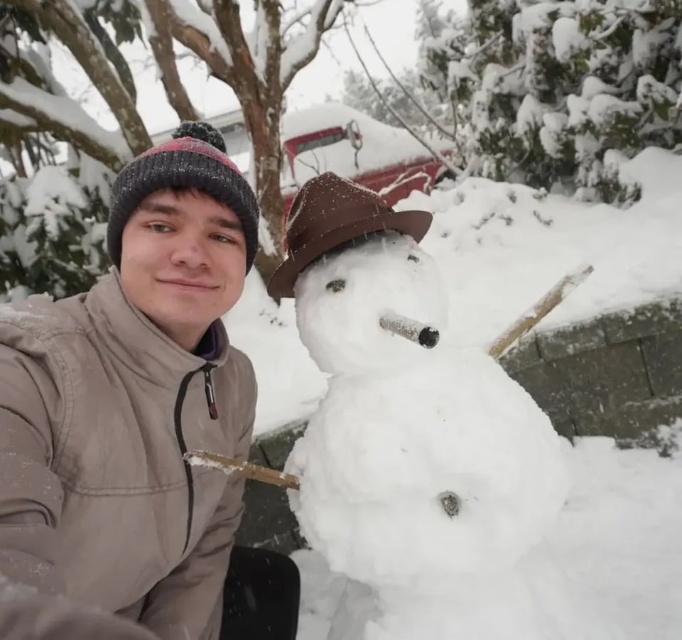 Stefan lächelt neben einem Schneemann in einer Winterlandschaft in Kanada