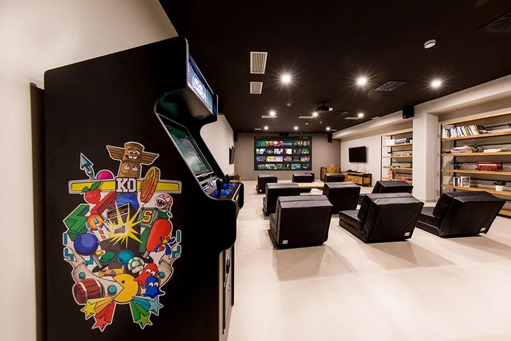 Sala de juegos de la residencia con máquina recreativa, televisión y sillones