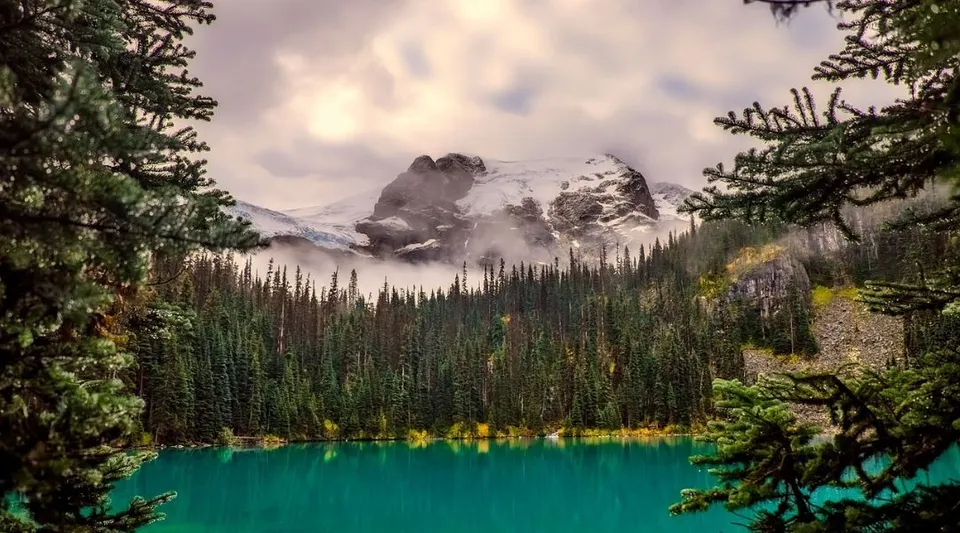 Un lago turchese circondato da una foresta di pini e montagne innevate nella regione del Perth & District Collegiate Institute.