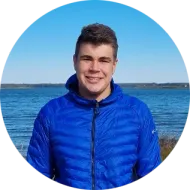 Estudiante sonriente con chaqueta azul delante de un lago
