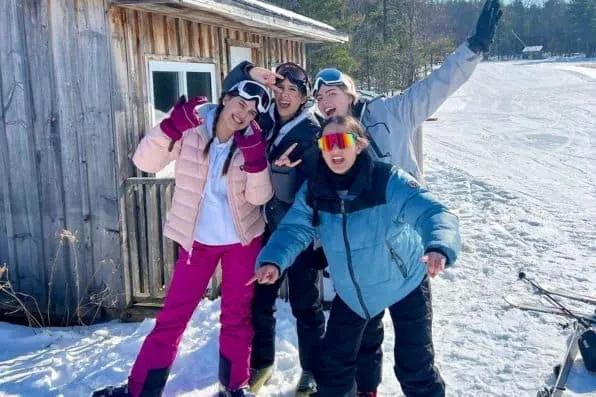 Cuatro jóvenes con ropa de esquí posan sonrientes en la nieve junto a una cabaña