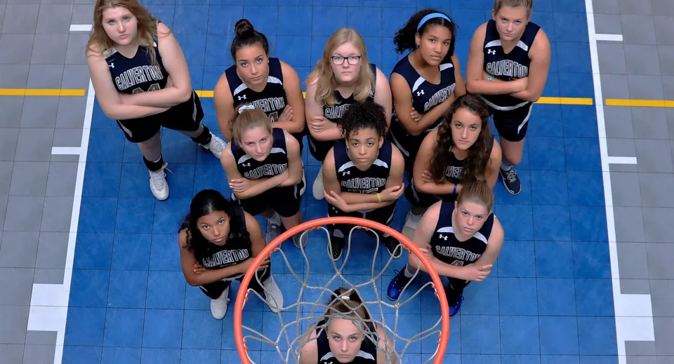 Un gruppo di giovani giocatrici di basket si trova sul campo da basket della The Calverton School con un canestro in primo piano.