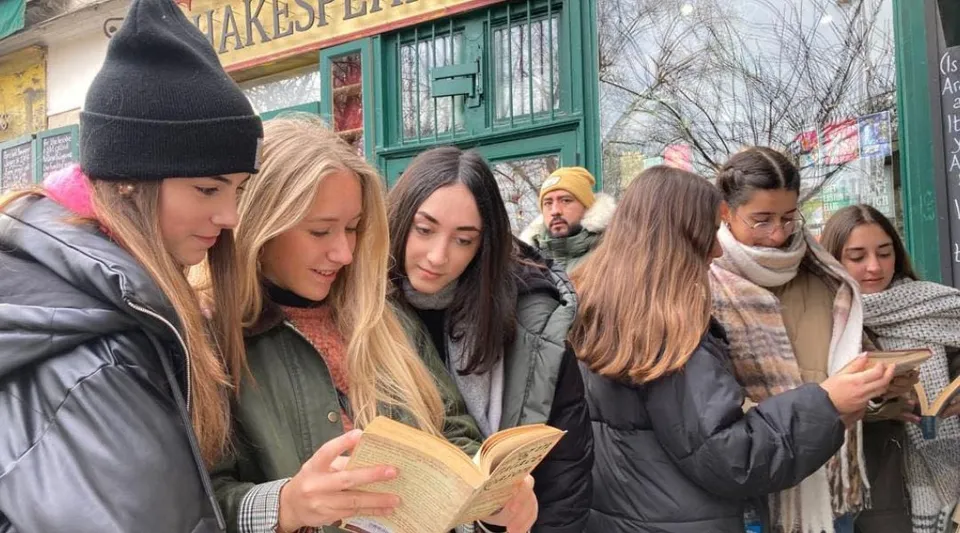 Un gruppo di studenti della San Vicente de Paul School si trova all'aperto davanti a un negozio: alcuni leggono libri, altri usano dispositivi mobili.