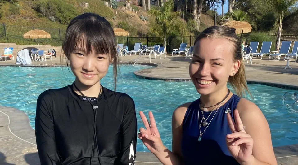 Due studentesse della Lake Tahoe Preparatory School mostrano sorridendo il segno della pace davanti a una piscina con palme.