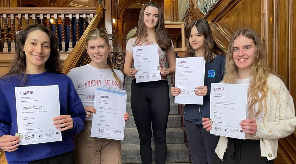 Cinque studentesse della Tring Park School for the Performing Arts mostrano i loro diplomi alla fotocamera in una stanza storica.