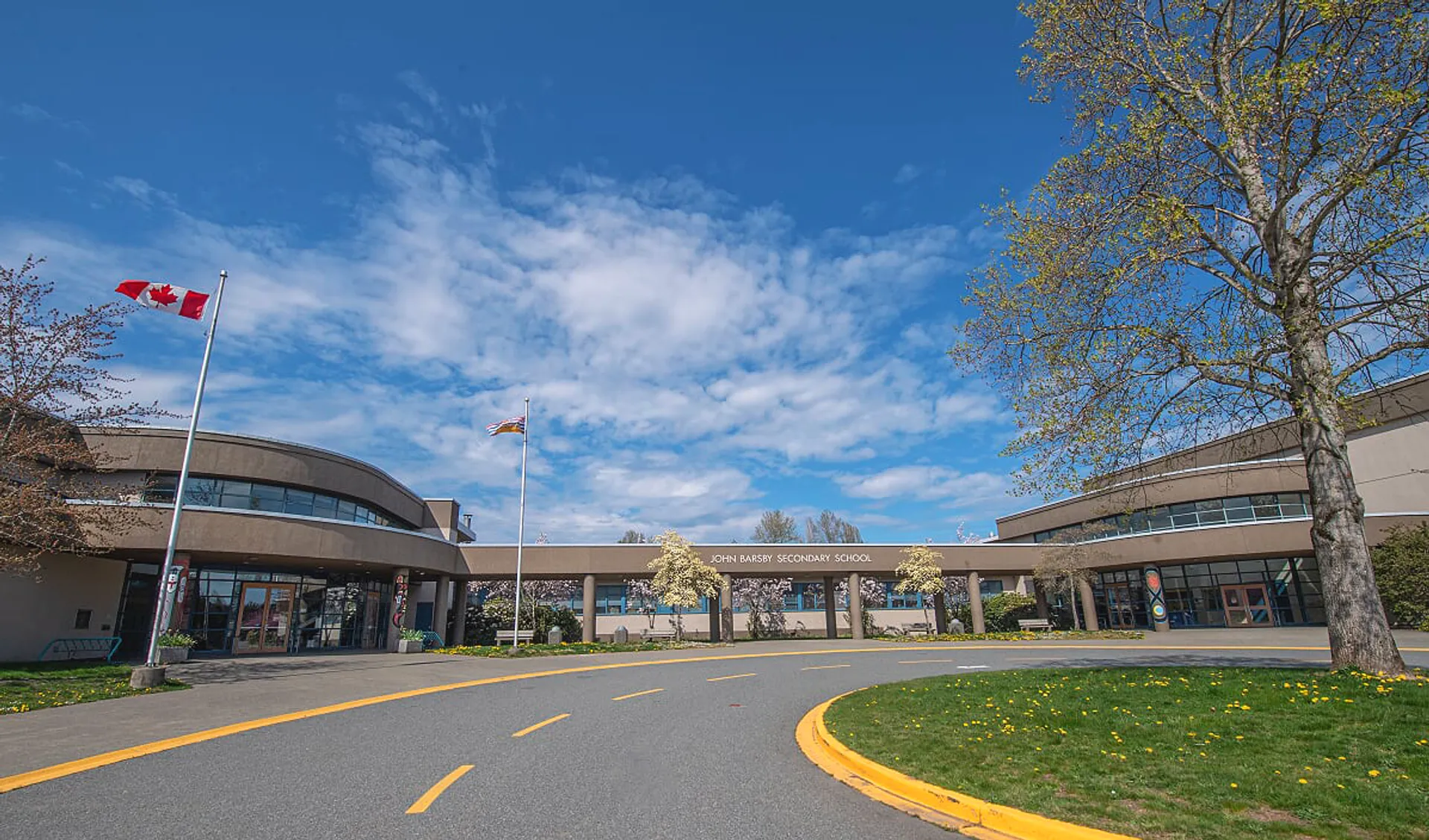 L'edificio moderno della John Barsby Secondary School è circondato da alberi e mostra una bandiera canadese su uno sfondo di cielo blu.