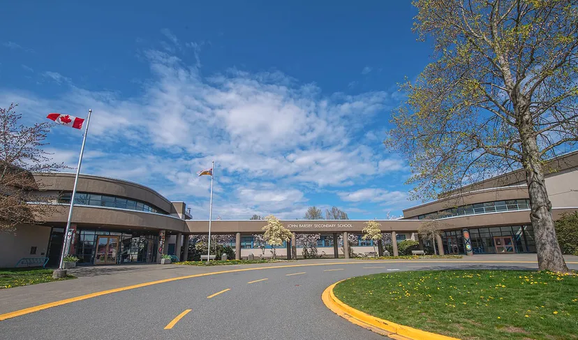 L'edificio moderno della John Barsby Secondary School è circondato da alberi e mostra una bandiera canadese su uno sfondo di cielo blu.