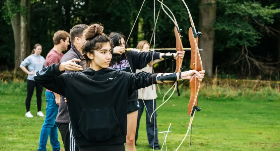 Studenti della Frensham Heights School praticano il tiro con l'arco su un campo di allenamento erboso.