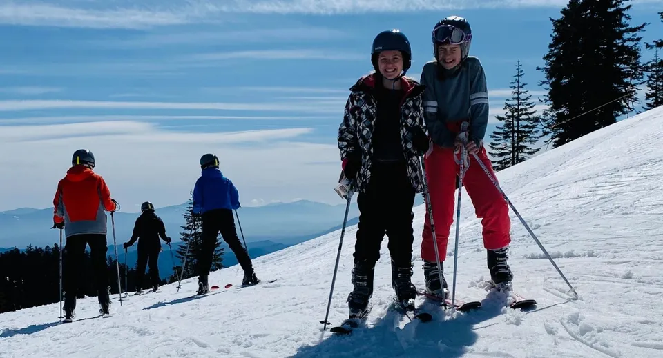 Un gruppo di studenti della New Hope Christian School scia su un pendio innevato con pini e cielo blu sullo sfondo.