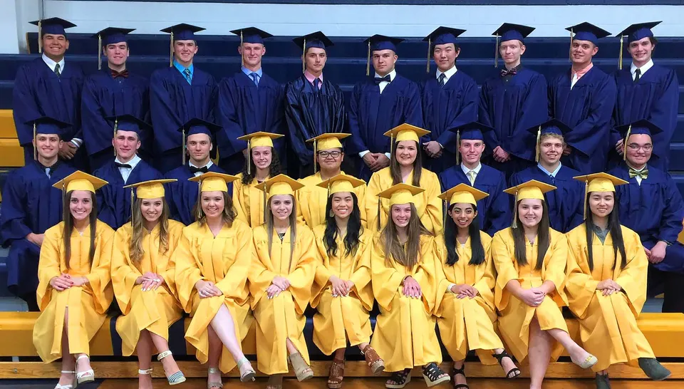 Diplomati e diplomate della Aquin High School in toghe blu e gialle davanti a uno sfondo giallo.
