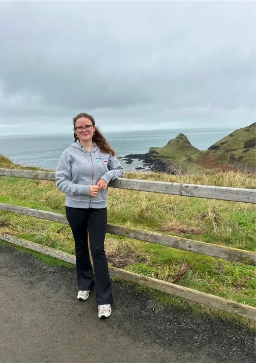 Olivia lächelt vor einer Felsküste am Ozean in Irland