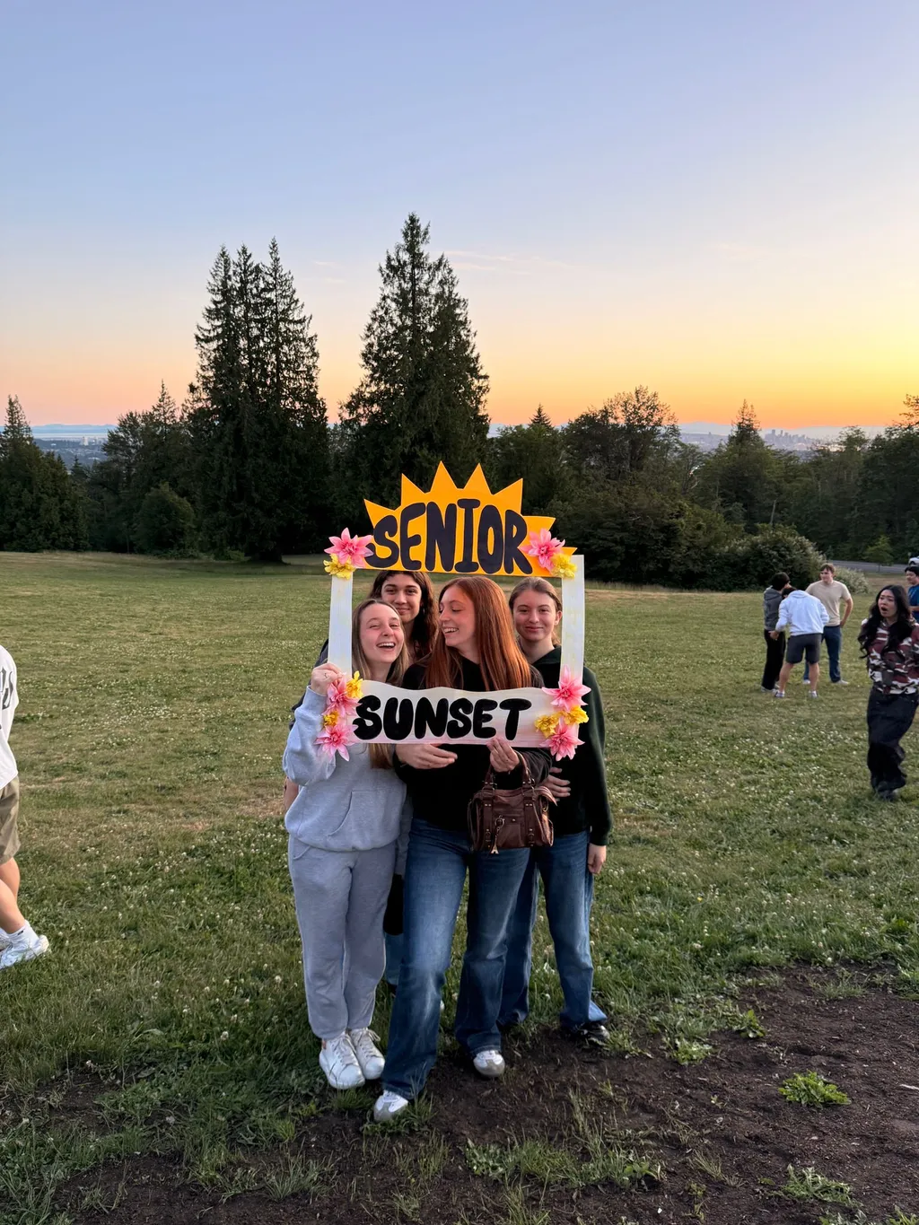 Studentesse posano con una cornice 'Senior Sunset' in un parco al tramonto in Canada