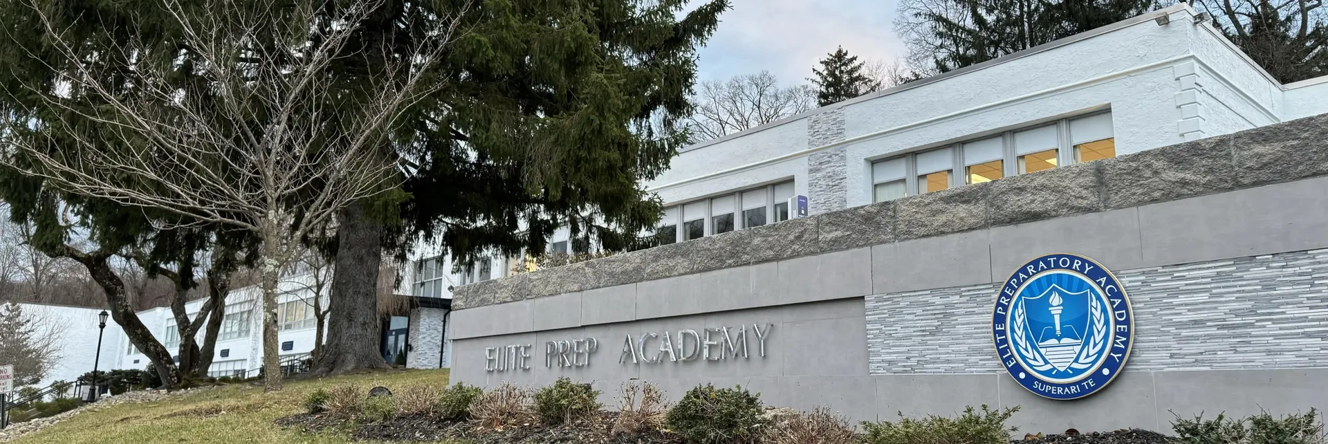 L'edificio della Elite Preparatory Academy con un muro di pietra e il logo della scuola in primo piano.