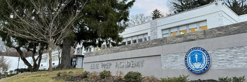 L'edificio della Elite Preparatory Academy con un muro di pietra e il logo della scuola in primo piano.
