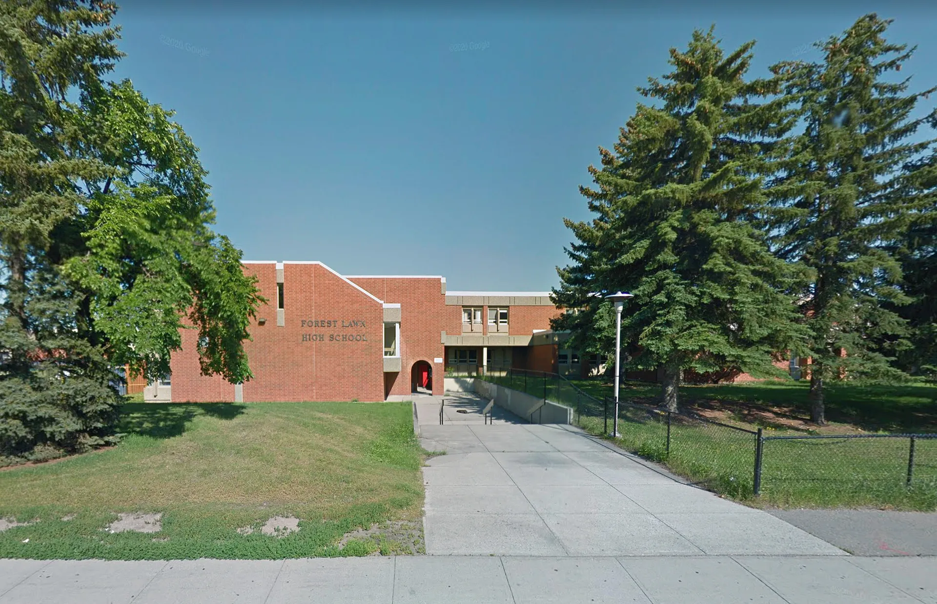 L'edificio in mattoni della Forest Lawn High School con il tetto rosso si erge circondato da alberi verdi sotto un cielo blu.