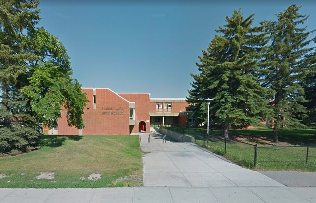 L'edificio in mattoni della Forest Lawn High School con il tetto rosso si erge circondato da alberi verdi sotto un cielo blu.